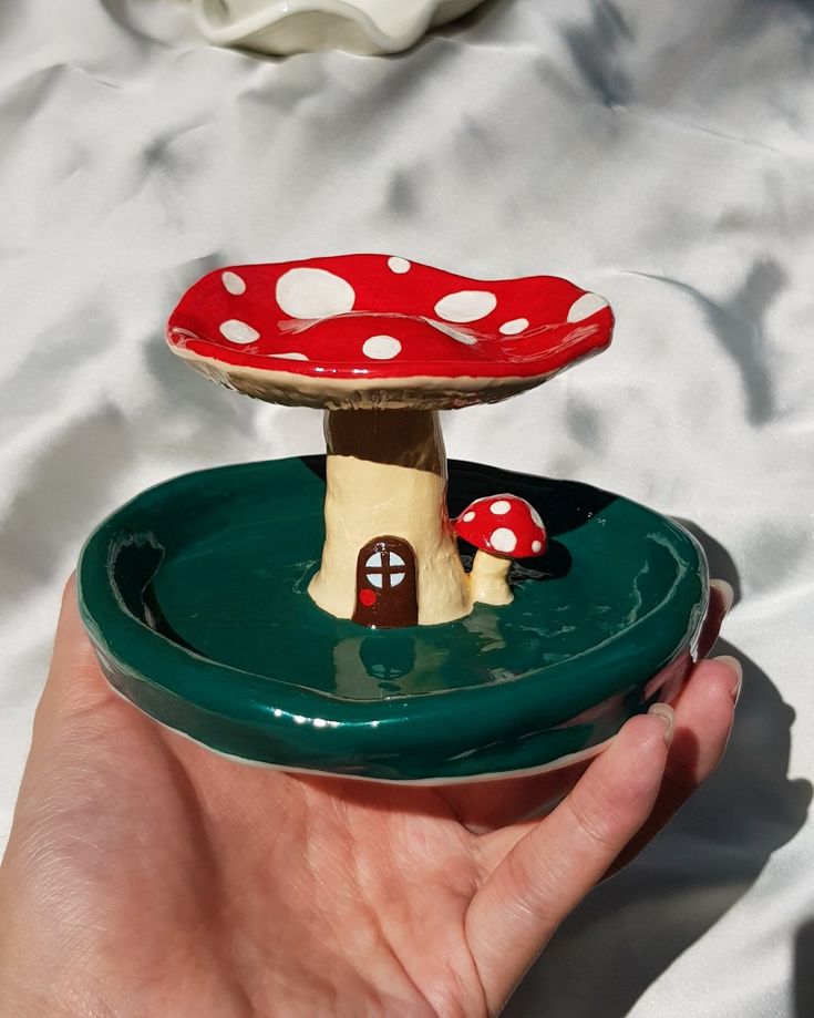 a hand holding a small mushroom house on top of a green plate