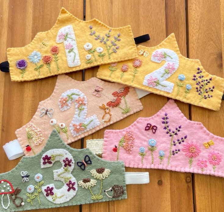 five handmade baby bibs with flowers and numbers on them sitting on a wooden floor