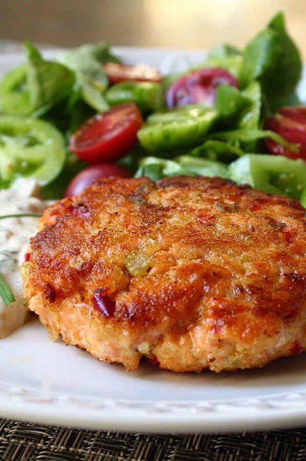 a white plate topped with meat patties next to a salad and dressing on a table