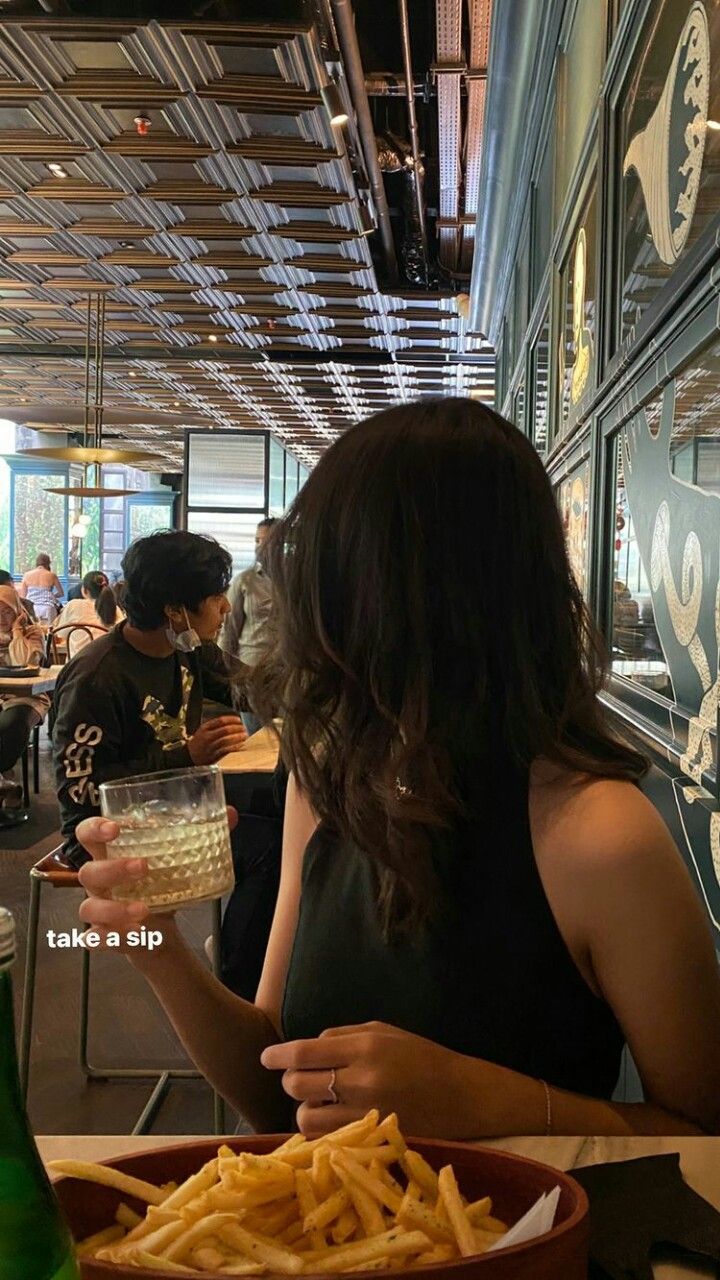 a woman sitting at a table with a plate of fries and a drink in her hand