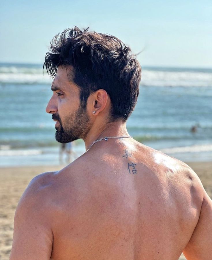 a shirtless man on the beach with his back turned to the camera, looking off into the distance