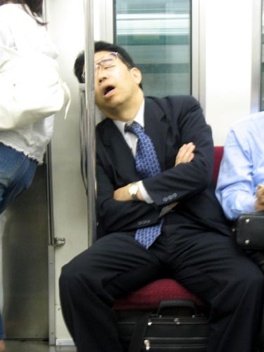 two people sitting on a train with their arms crossed and one person standing next to them