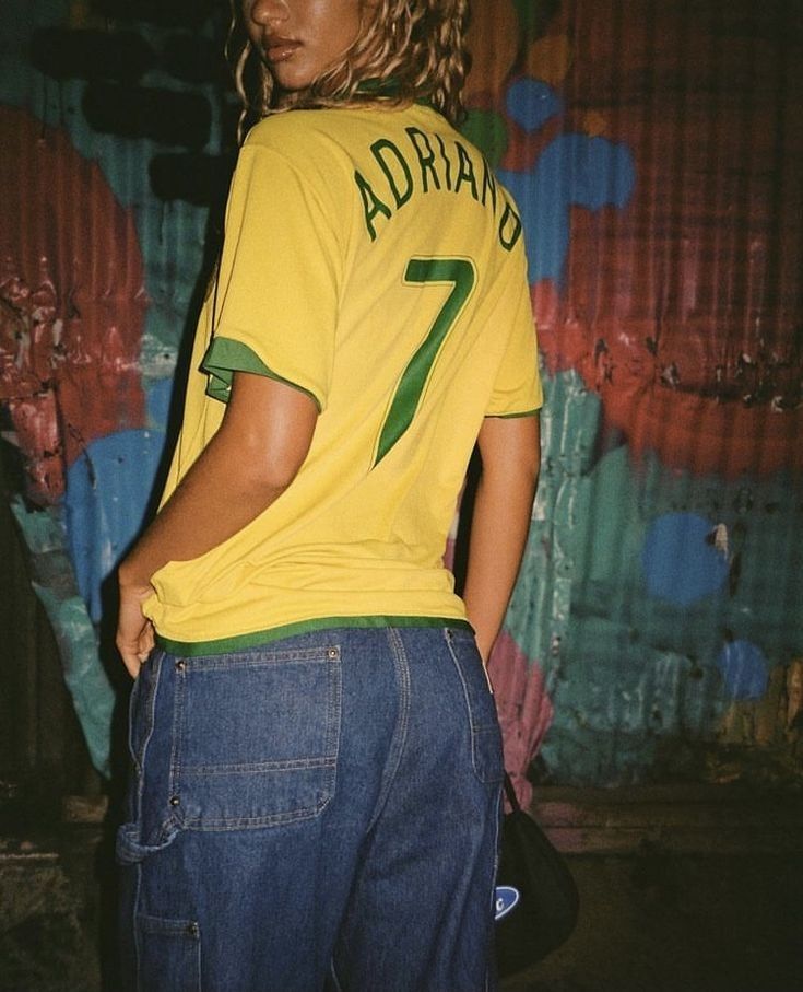 a woman wearing a yellow shirt and jeans standing in front of a graffiti covered wall