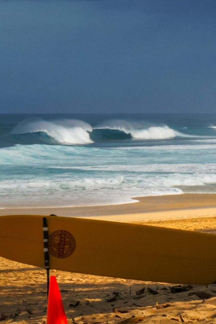 a surfboard leaning up against a pole on the beach with waves in the background