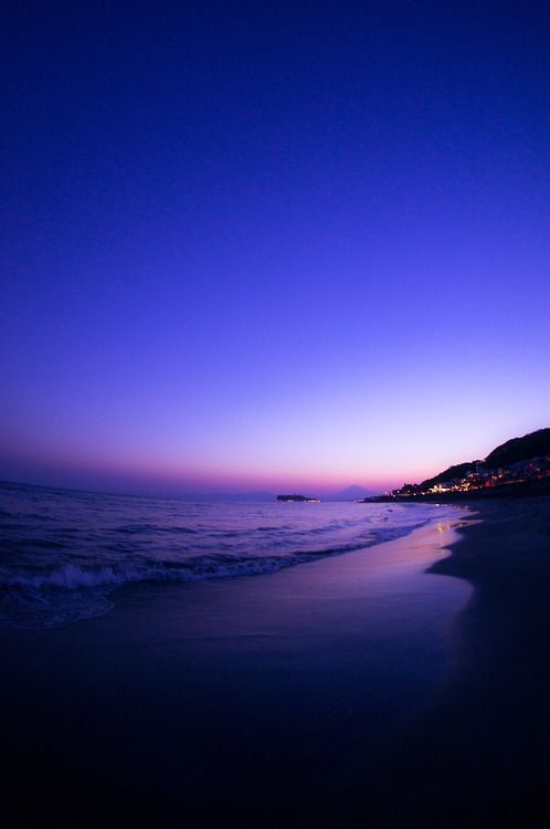 the beach at night with some buildings in the distance and water on the shore line