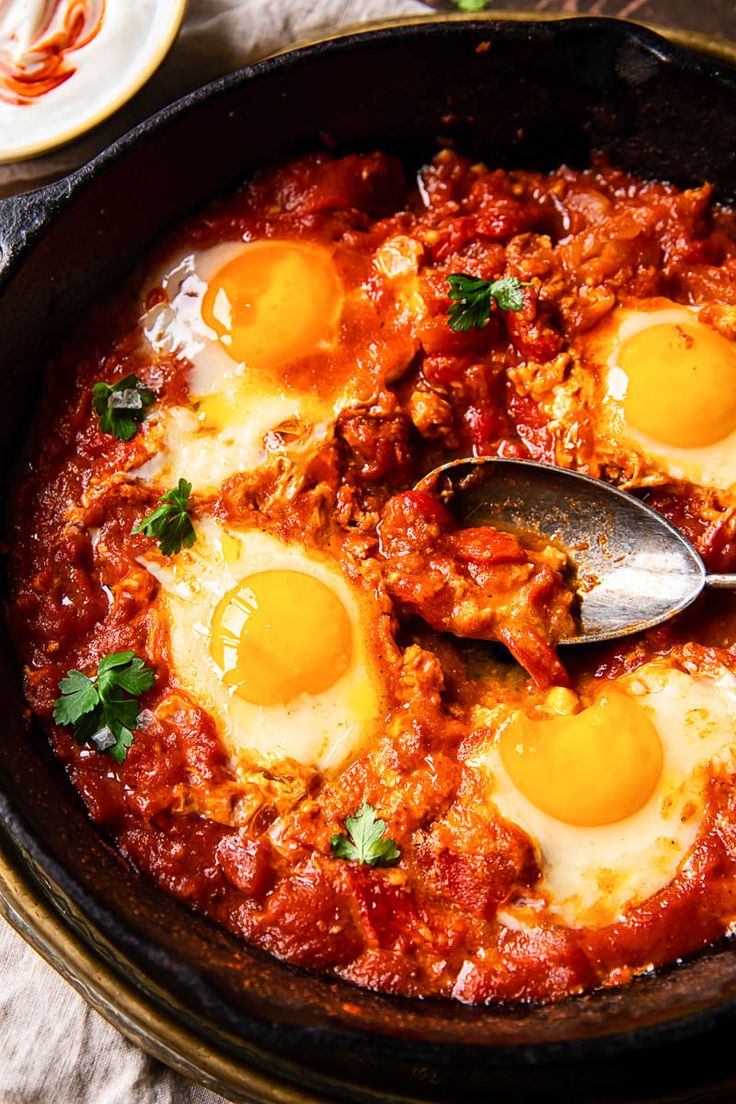 two eggs are being cooked in a skillet with sauce and parsley on the side