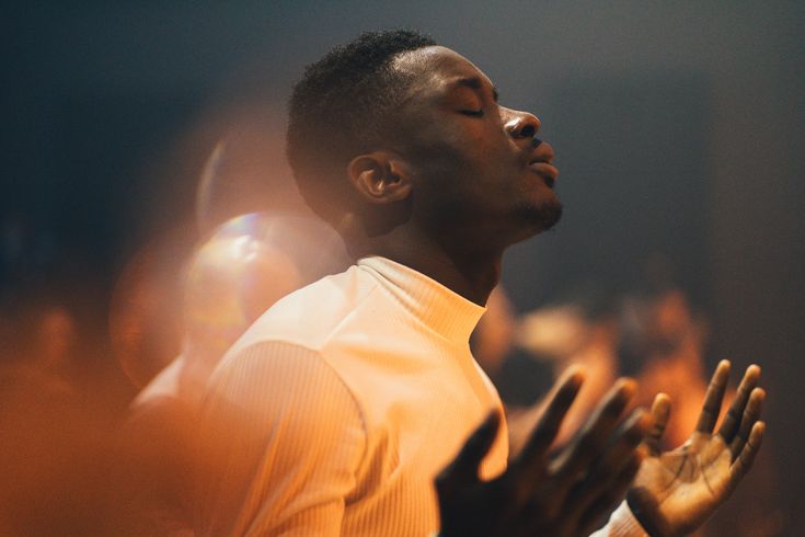 a man standing in front of a crowd holding his hands up to the sky and praying