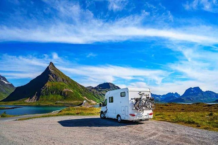 an rv parked on the side of a dirt road next to water and mountains in the background