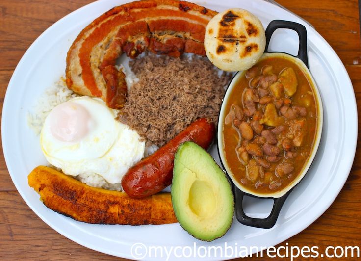 a white plate topped with lots of food on top of a wooden table next to a cup of coffee