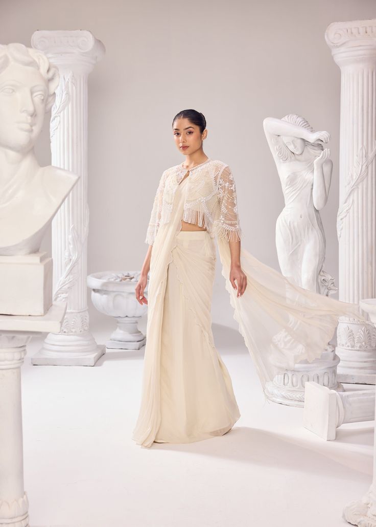 Our rich craftsmanship adorn the jacket. The organza saree has scallops on all the corners of the drape, paired with an organza plunge neckline sleeveless blouse. Get ready to make a statement with this effortless silhouette, delicate embroidery and the soothing hue. Colour: Off- White Material: Net- Jacket, Organza- Saree, Organza- Blouse No of components: 3 Surface Ornamentation: Hand Embroidery Care Instructions: Dry Clean Shipping Time: 3-4 weeks Elegant Chanderi Pre-draped Saree For Evening, Wedding Chanderi Pre-draped Saree, Elegant Silk Pre-draped Saree For Wedding, Elegant Festive Sheer Blouse, Elegant Pre-draped Saree With Chikankari For Reception, Elegant Pre-draped Chikankari Saree For Reception, Wedding Blouse With Draped Resham Embroidery, Wedding Blouse With Resham Embroidery And Draped Shape, Elegant Draped Chanderi Saree