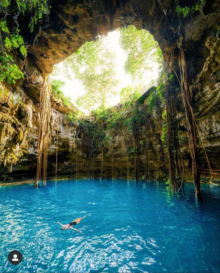 a man swimming in a blue pool surrounded by greenery and rock formations, with an arch opening to the water