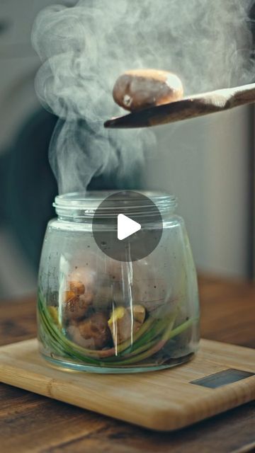 a person stirring food in a glass jar with steam rising from the top, on a cutting board