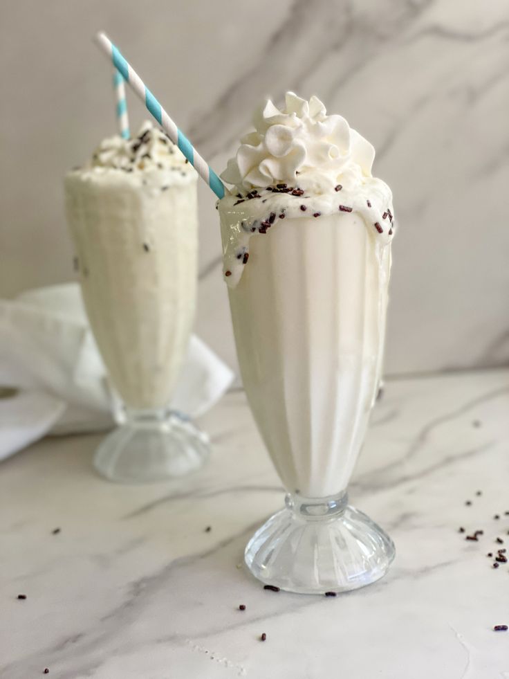 two milkshakes with whipped cream and chocolate sprinkles are on the table