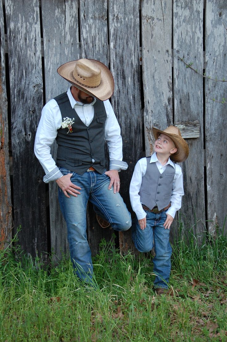 a man and boy wearing cowboy hats standing in front of a wooden fence