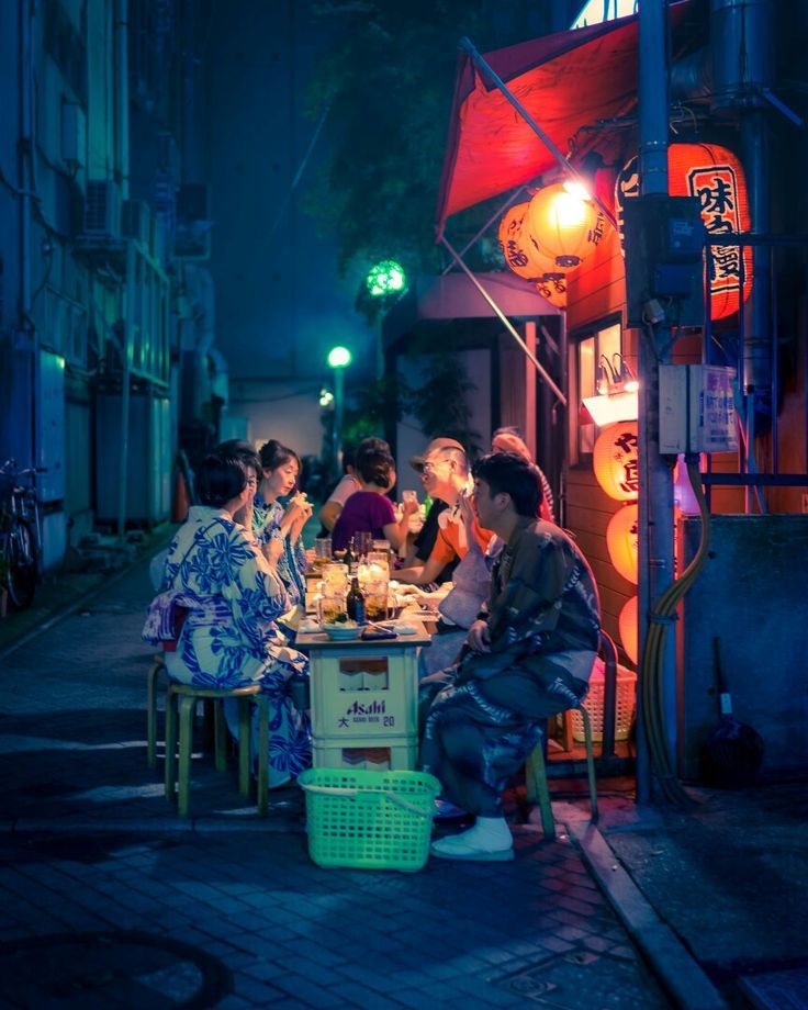 group of people sitting around a table in the middle of an alleyway at night