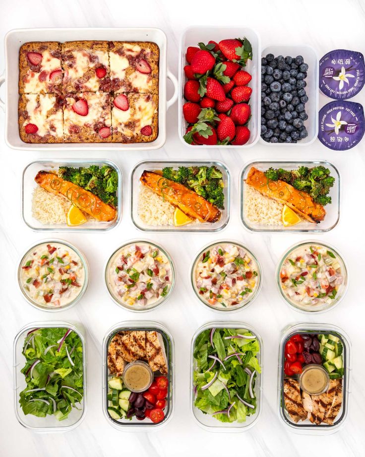 a variety of food in plastic containers on a white counter top with blueberries, strawberries, and other foods