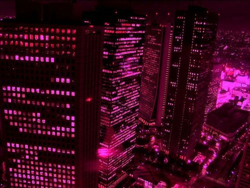 an aerial view of some very tall buildings in the city lit up with pink lights