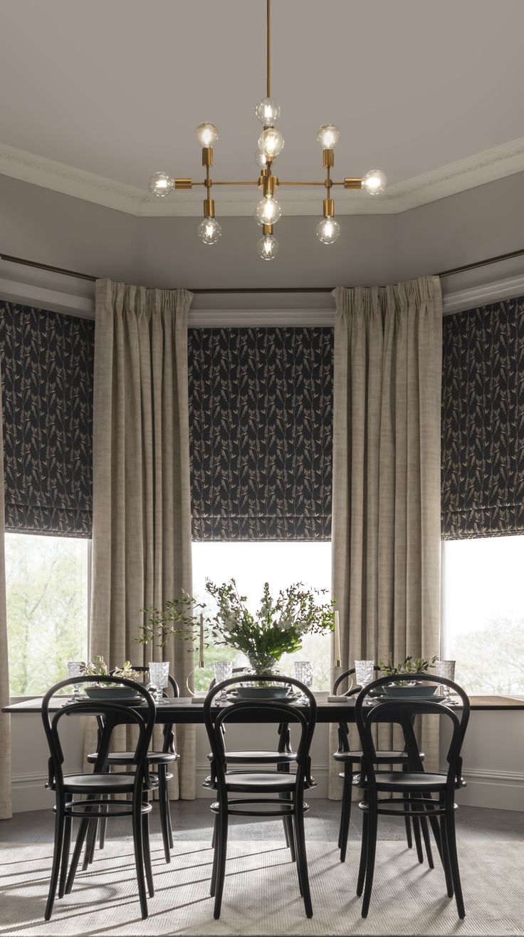 a dining room table with four chairs in front of two windows covered by drapes