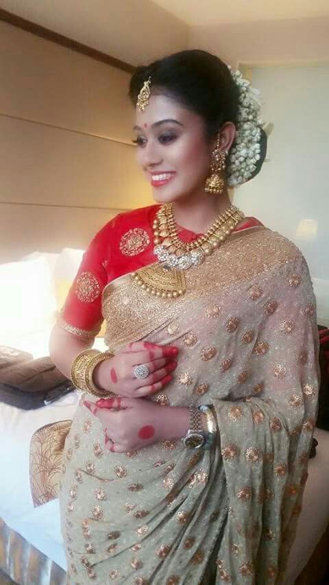 a woman in a red and gold sari is standing near a bed with her hands on her stomach