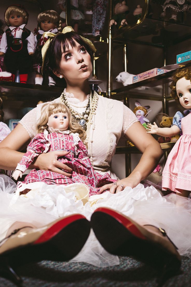 a woman sitting on top of a bed holding a doll next to two other dolls