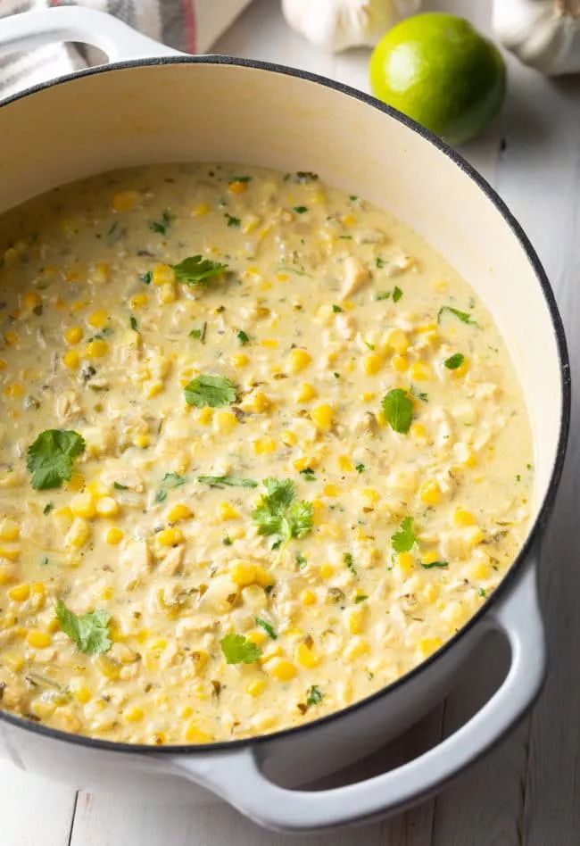 a pot filled with corn and cilantro on top of a table next to limes