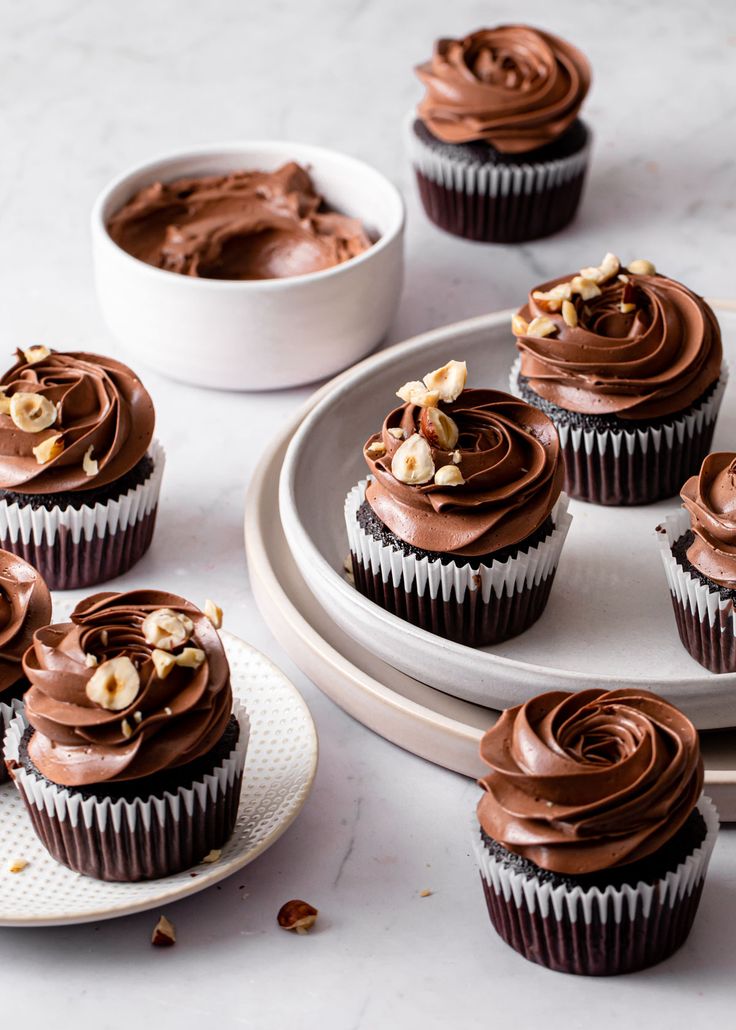 cupcakes with chocolate frosting and walnuts on a white plate next to a bowl of nuts