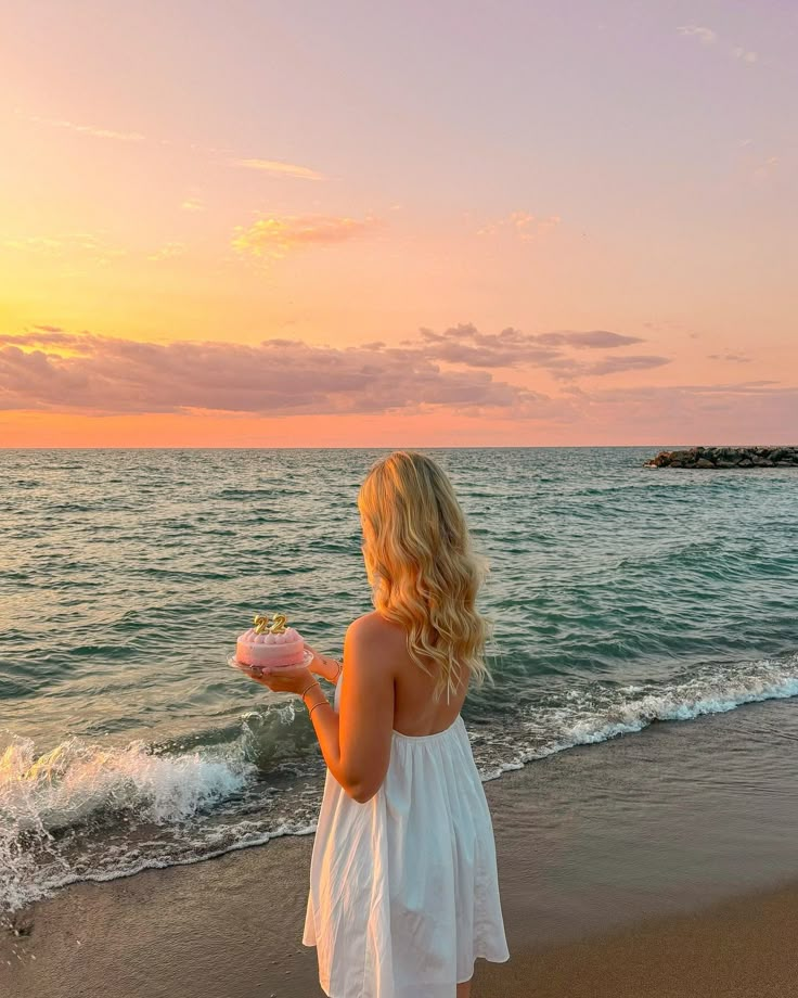 a woman standing on top of a beach holding a cake