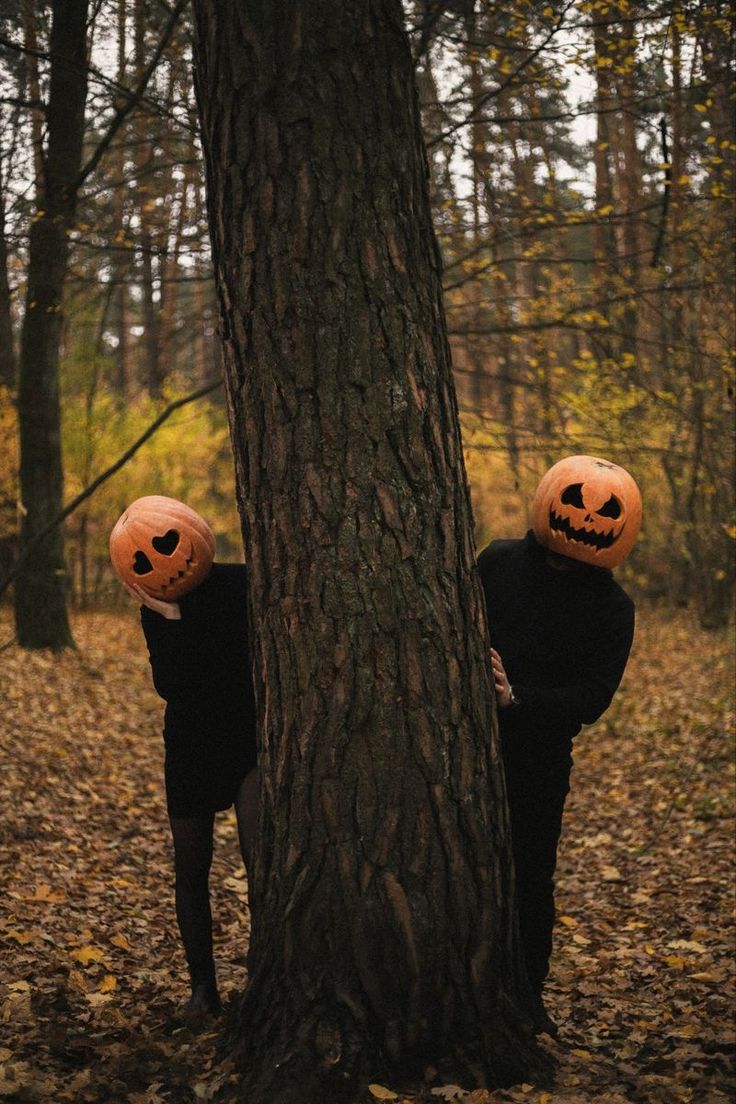 two people wearing pumpkin heads standing next to a tree