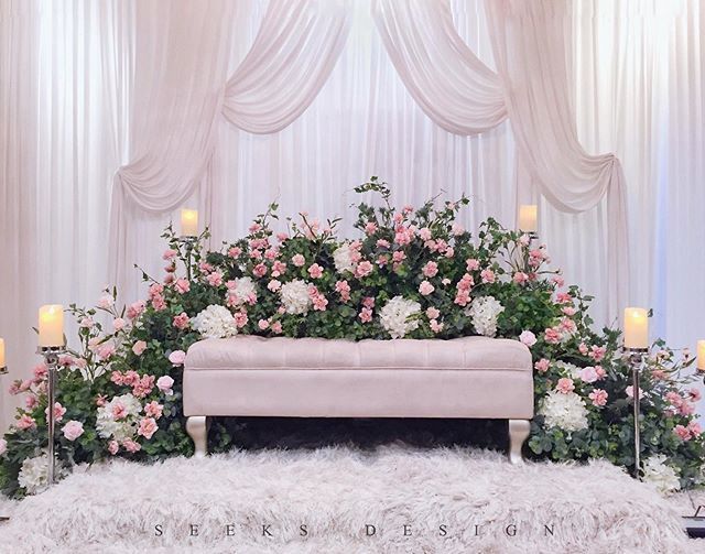 a pink bench with flowers and candles in front of a white curtained backdrop for a wedding