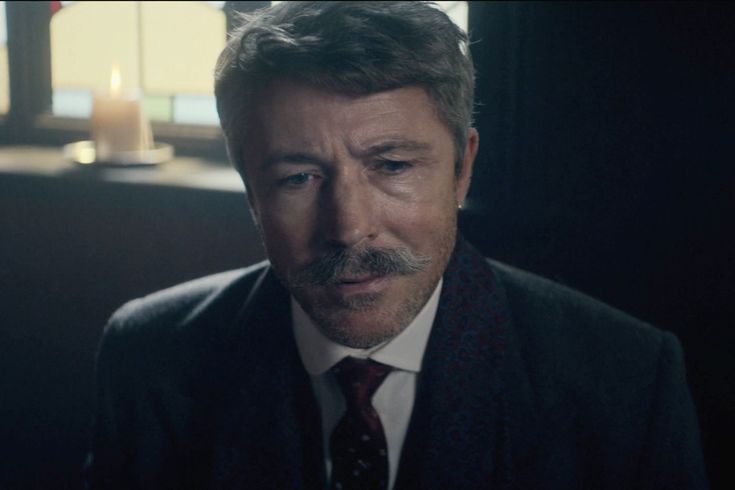 a man wearing a suit and tie looking at something in the distance with a candle lit behind him