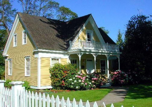 a yellow house with white picket fence and flowers