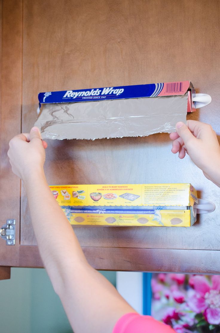 a person holding a toothbrush in front of a box of toothpaste on top of a cabinet