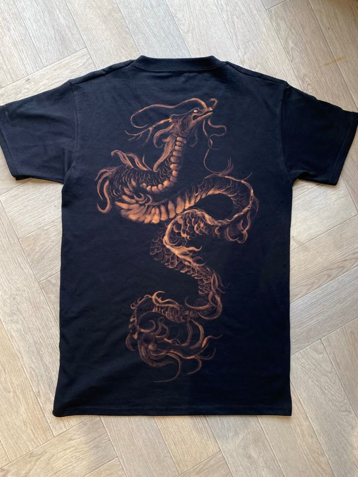 a black t - shirt with an orange dragon on the front and back, sitting on a wooden floor