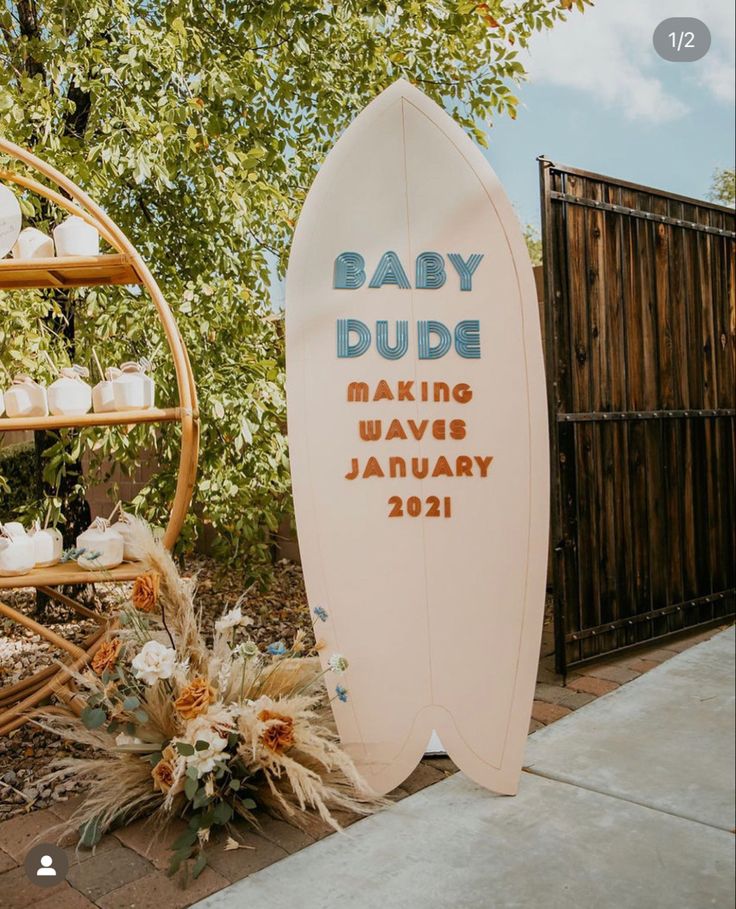 a baby dude sign next to a surfboard with candles and flowers on the ground