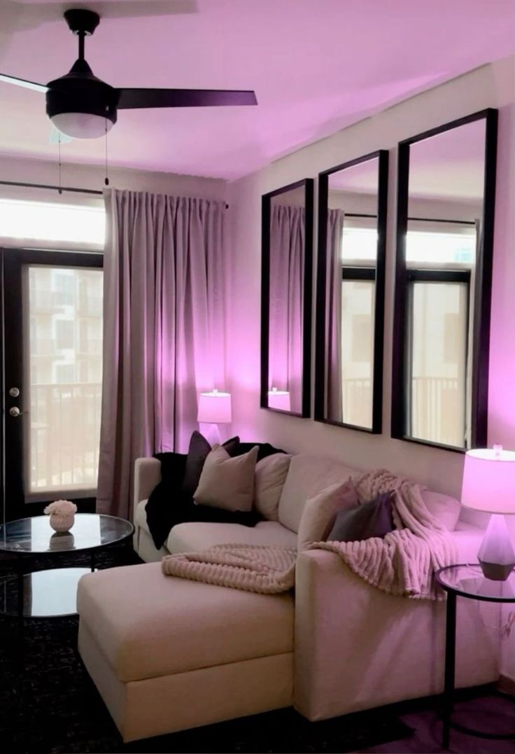 a living room filled with furniture and pink lighting on the walls, along with large windows