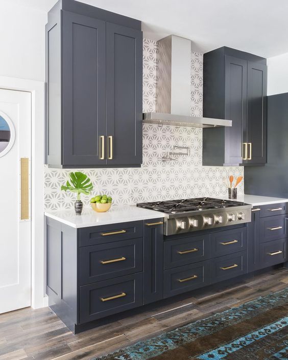 a kitchen with dark blue cabinets and white counter tops, gold trim on the drawers