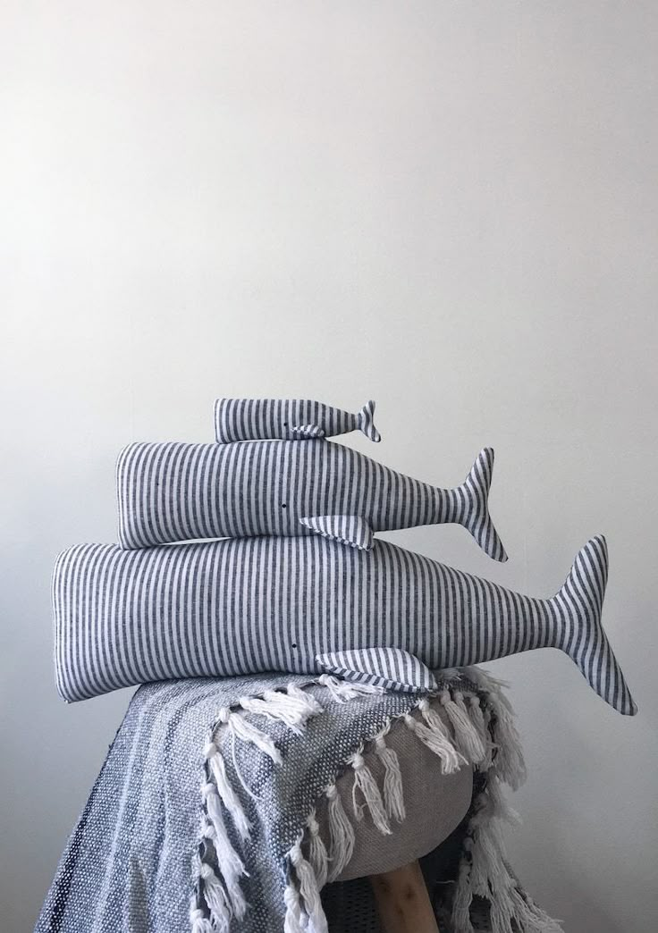 a pile of pillows sitting on top of a wooden stool next to a wall with a white and blue striped pillow