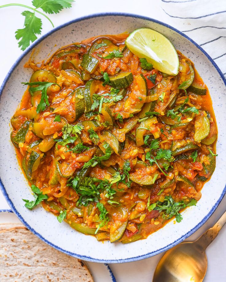 a white bowl filled with vegetable curry next to bread and a lime wedge on the side