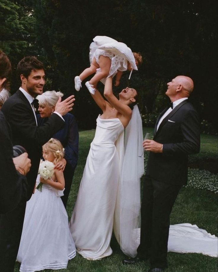 a woman in a wedding dress is holding up a small child while other people look on