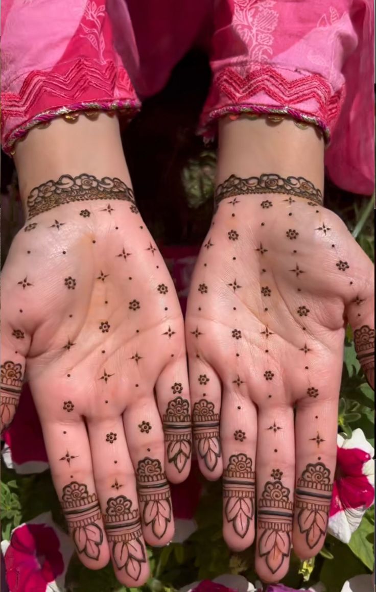 two hands with henna tattoos on them and flowers in the background, both holding their hands together