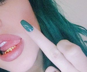 a close up of a person with green hair pointing to the side and wearing gold teeth