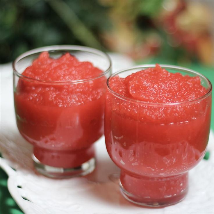 two glasses filled with red liquid sitting on top of a white plate next to each other