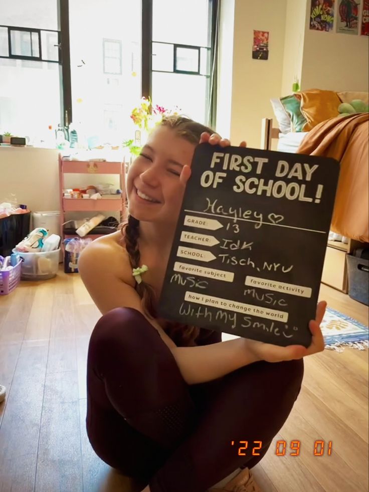 a young woman holding up a sign that says first day of school on the board