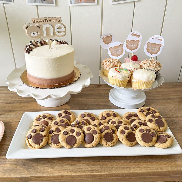 a table topped with lots of cookies next to a cake and cupcakes on plates