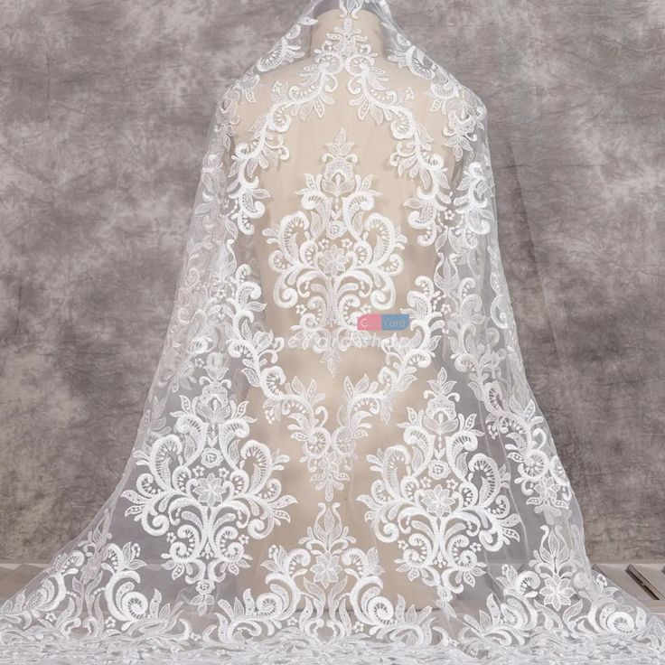 the back of a white wedding veil with an intricate lace pattern on it, hanging from a mannequin's head