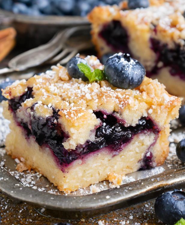 a piece of blueberry crumb cake on a plate with powdered sugar and fresh berries