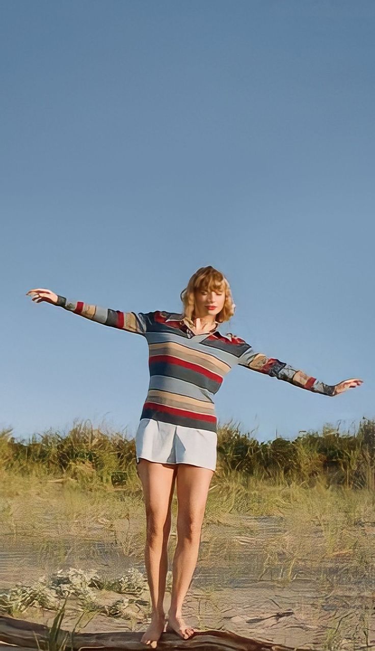 a woman standing on top of a wooden log in the middle of a sandy field