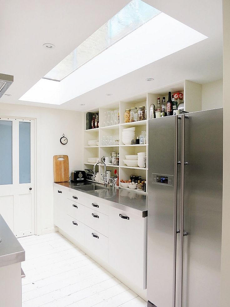 a kitchen with white cabinets and stainless steel appliances in the center, under a slanted skylight