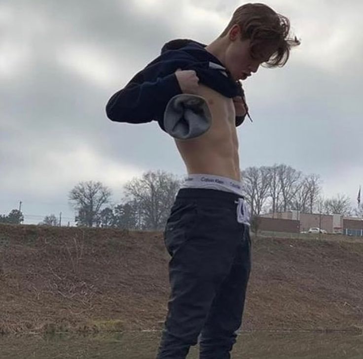 a man standing on top of a skateboard next to a dirt field with trees in the background