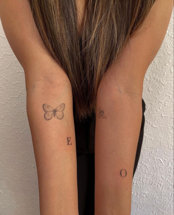 two girls with matching tattoos on their arms, one has a butterfly and the other has an e